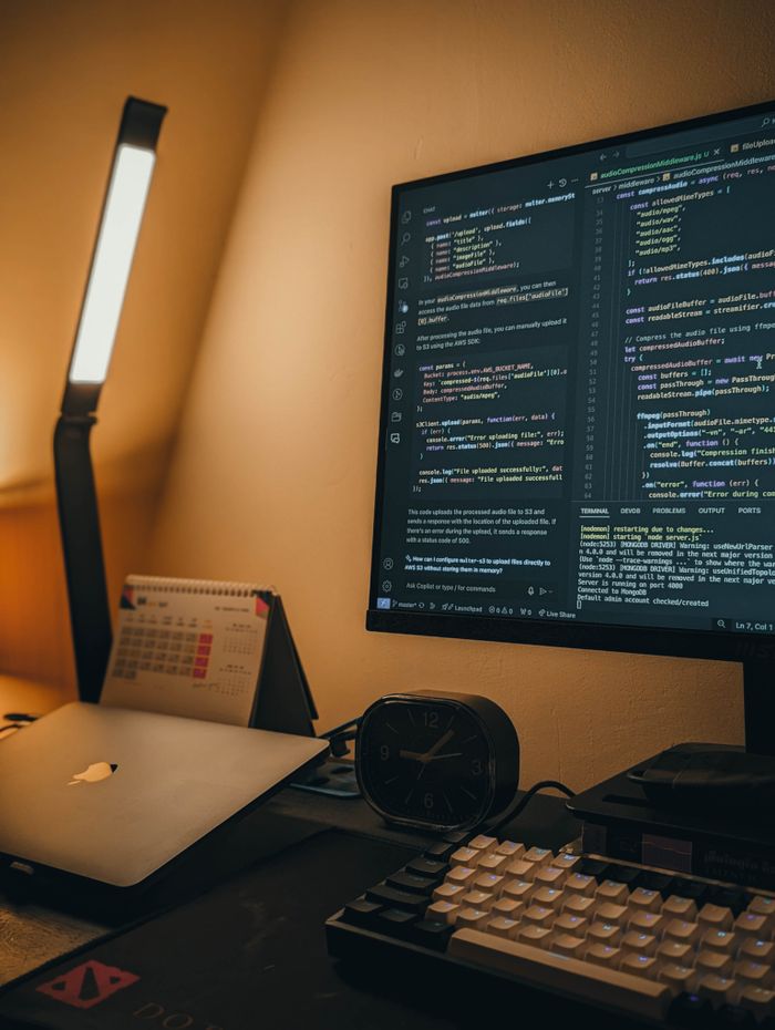 A well-lit home office setup featuring a coding monitor, laptop, and desk accessories.